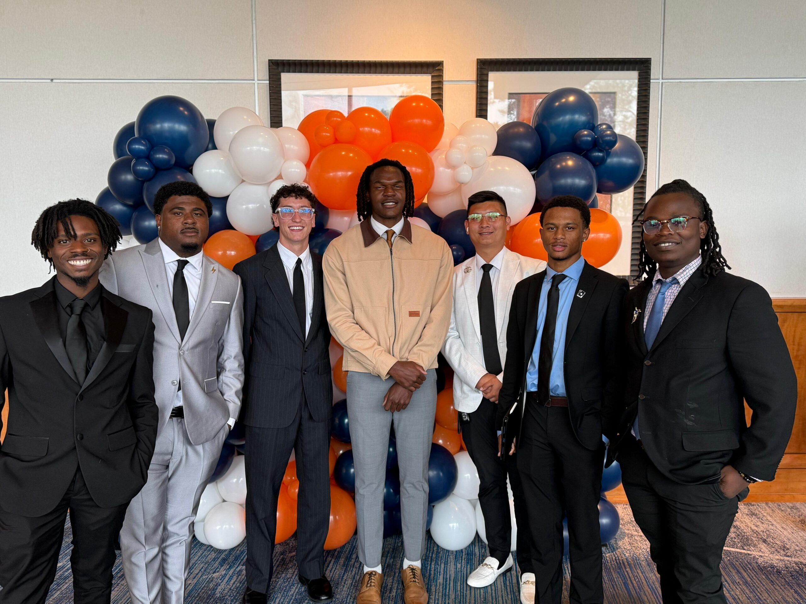 Seven team members in business attire standing before a colorful balloon display