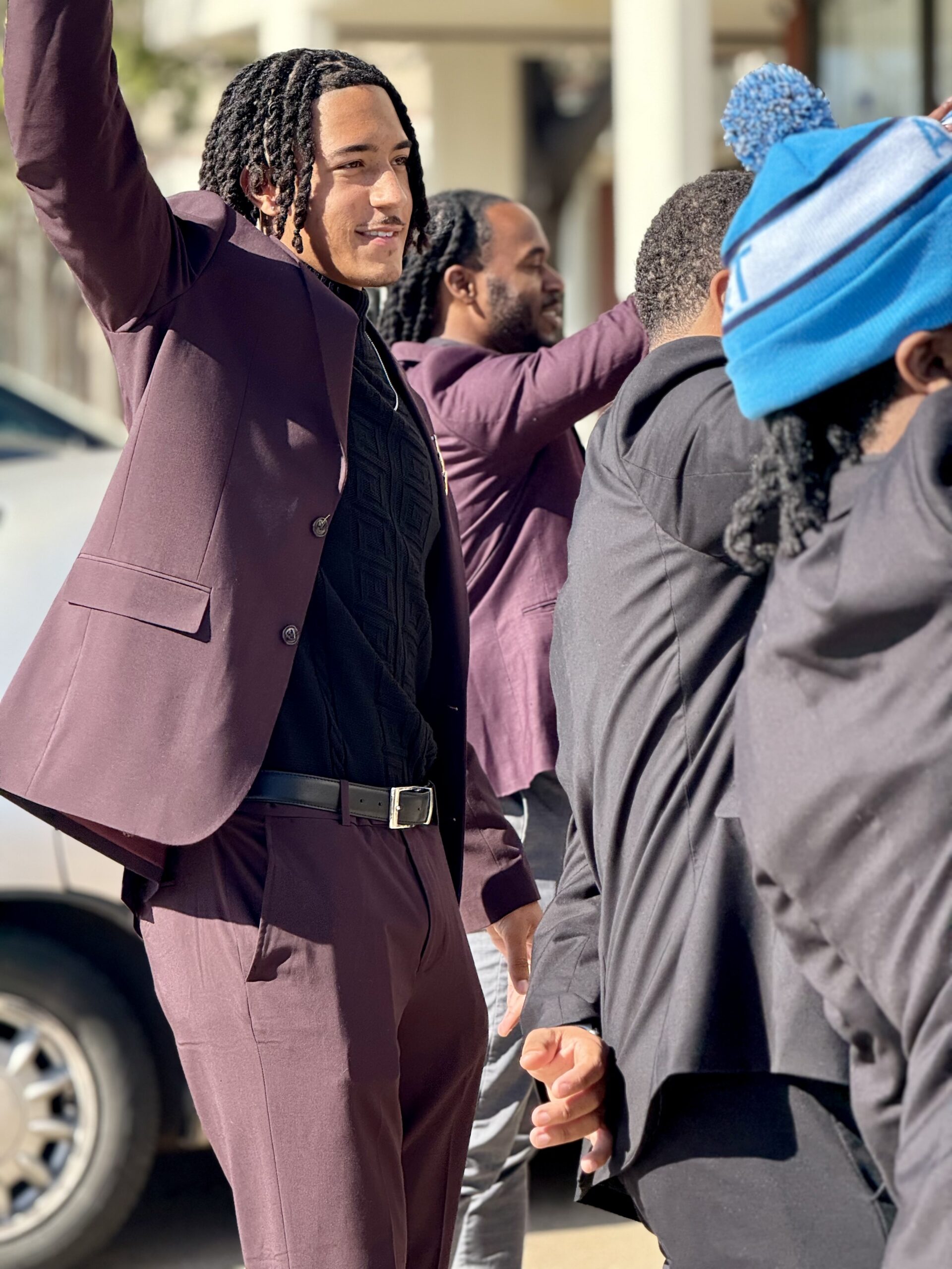 Team member in a purple suit celebrating with raised hands outdoors